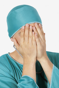 一位心烦意乱的男外科医生用手在灰色背景下遮住脸
