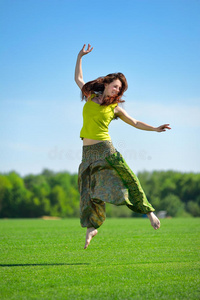 在绿色草地上跳跃的年轻女子