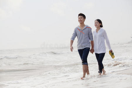 一对年轻夫妇手牵着手在海边散步，中国