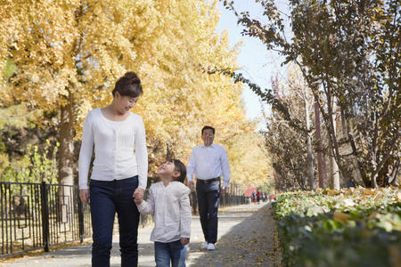 秋天，爷爷奶奶和孙女手牵着手走在公园里