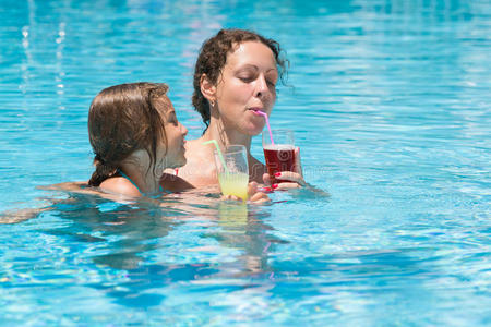 母女俩在游泳池里喝果汁。