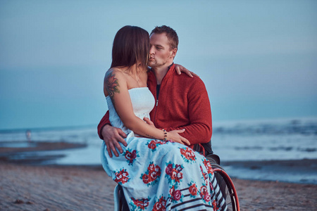 一对爱的情侣, 一个女人坐在她的丈夫膝上, 在海滩上亲吻一个明亮的黎明背景