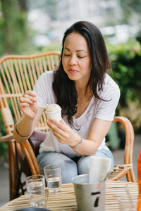 一个泛亚洲女人的肖像, 在咖啡和冰淇淋的咖啡馆里, 在阳光下放松。她坐在藤椅上, 微笑着, 而她享受下午