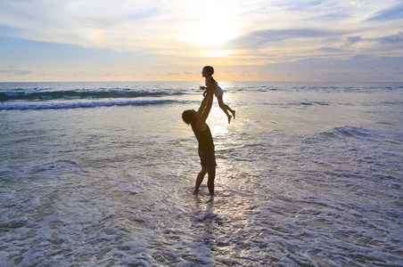 父亲的剪影投掷小女儿在海滩在日落