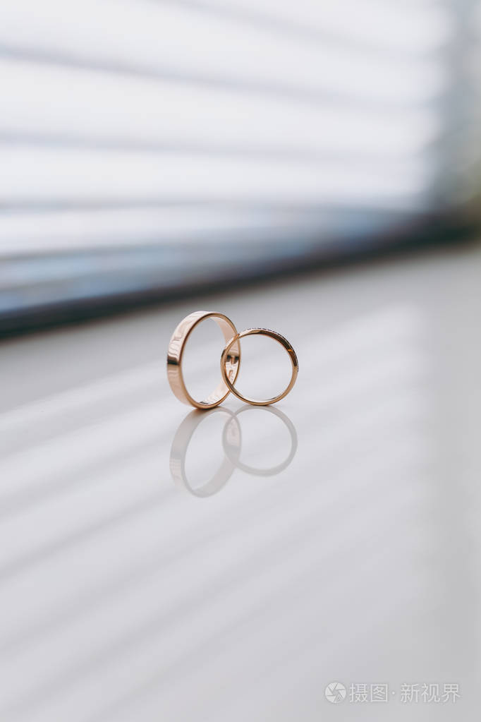 关闭两个美丽的时尚金色结婚戒指新娘和新郎相交在一个白色的光泽窗台