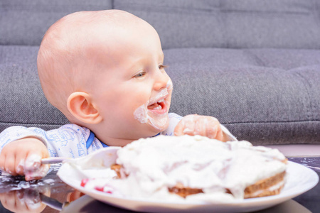 一个小男孩的第一个生日庆祝。小男孩用勺子吃生日蛋糕, 生日快乐。孩子在餐桌上的蛋糕。小宝宝粉碎生日蛋糕