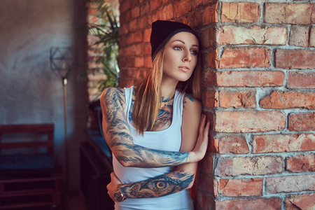 一个 tattoed 的金发女郎在 t恤和帽子摆在砖墙上