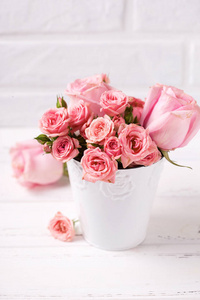 粉红色的玫瑰花在白色的锅对白色砖墙。花静物。选择性对焦。文本的位置。垂直图像