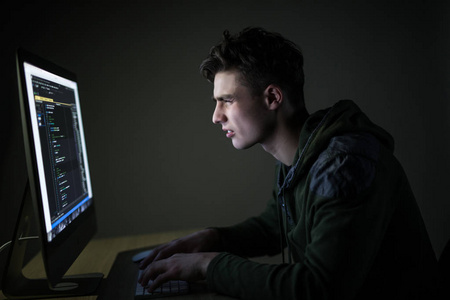 年轻人在黑暗的房间里窃听服务器。年轻人程序代码在个人计算机在黑暗的房间。白色黑客