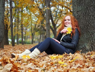 叶在城市公园的红发女孩的秋天