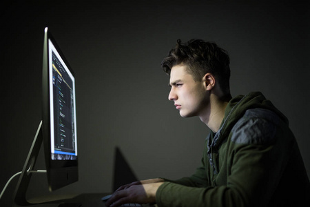 年轻人在黑暗的房间里窃听服务器。年轻人程序代码在个人计算机在黑暗的房间。白色黑客