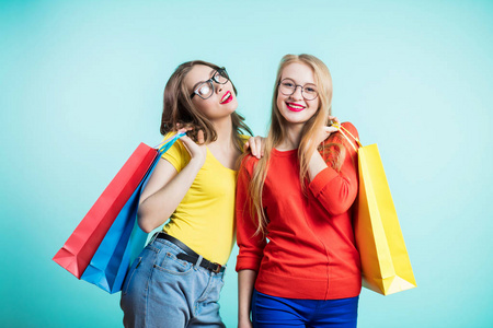 两个快乐的年轻妇女与购物袋在蓝色背景看着微笑。销售, 购物, 旅游和快乐的人