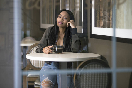 在咖啡店或人行道咖啡馆里有咖啡的黑人女性的窗口视图。企业家在休息或学生是耐心等待, 看起来独立