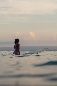 夕阳下的女性冲浪者坐在冲浪板上的后景色