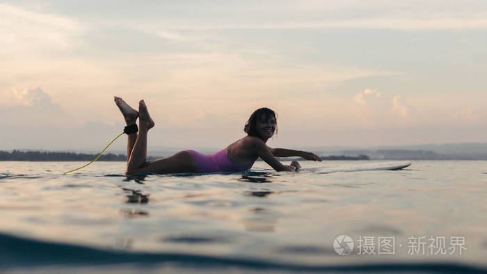 日落时分, 在海洋中的水冲浪板上躺着的女人剪影