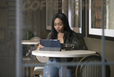 在咖啡店中使用连接到 wifi 互联网的平板电脑的黑色女性的窗口视图。女商人或学生在咖啡馆休息或工作和学习。