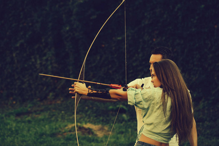 可爱的女孩和英俊的男人用弓和箭射击