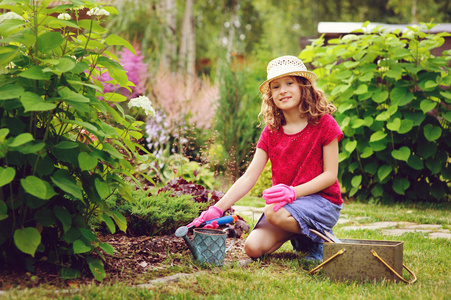 女孩玩小园丁, 并帮助在夏季花园, 戴着帽子和手套, 使用工具