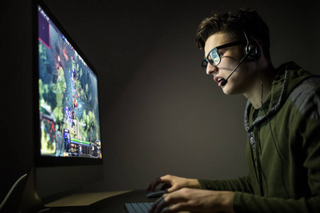 房间在线英俊的人玩策略或在线游戏在黑暗的房间在夜间照片