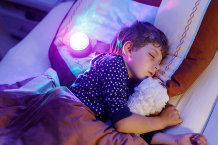 用彩色灯在床上睡觉的小学龄前孩子男孩
