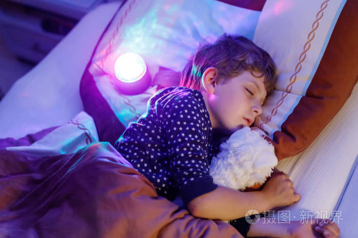 用彩色灯在床上睡觉的小学龄前孩子男孩