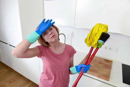服务女人在家庭厨房中携带清洁扫帚和拖把沮丧的手套
