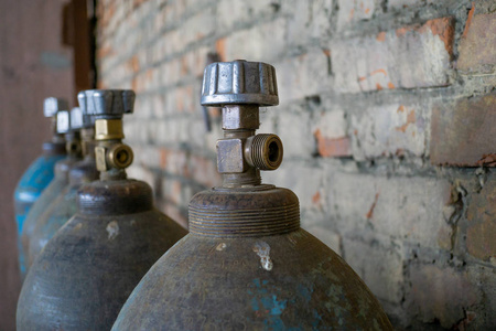 储存氧气和其他气体的旧磨损储罐站在废弃仓库的砖墙附近。