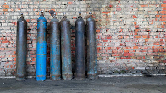 储存氧气和其他气体的旧磨损储罐站在废弃仓库的砖墙附近。