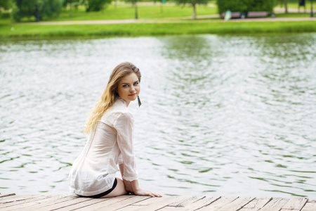 在白色外衣的年轻漂亮的女孩坐在一个木制的码头上 t