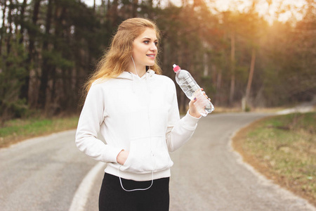 渴了的女人。年轻 漂亮的红发肖像体育女孩饮用水在公园的道路上。健身女人