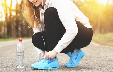 赛跑运动员的女孩。年轻的肖像体育女孩绑鞋带的道路上。健康的生活方式和运动的概念