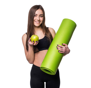微笑的年轻女子捧着画像卷起运动瑜伽垫和孤立的白色背景上的绿色苹果