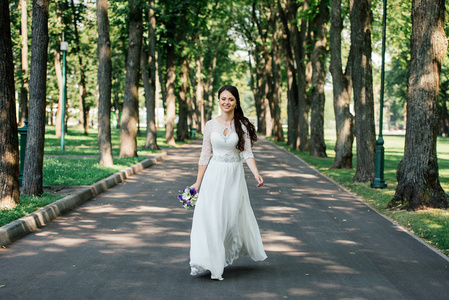 美丽年轻的微笑黑发的新娘的婚纱与手中的花束在户外公园里去