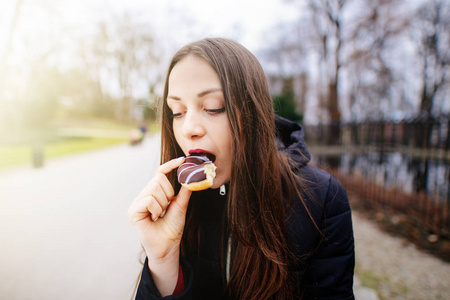 年轻漂亮的女孩吃甜甜圈在公园背景和微笑