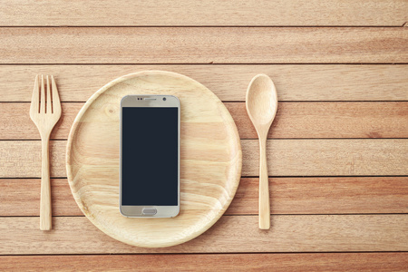木板背景上的木制盘子上的俯视智能手机
