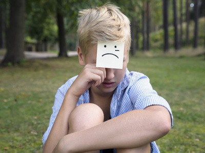 哭喊的男孩坐在森林的绿色草地上.悲伤的思想观念照片