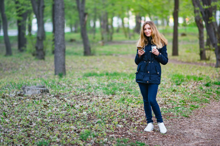 一个女孩走在早上在公园与智能手机和咖啡