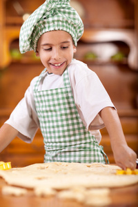 快乐微笑的小男孩厨师在厨房里做面团
