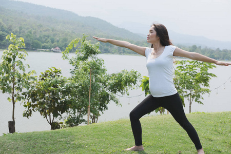 亚洲孕妇练瑜伽在公共 pa 的绿色草地上