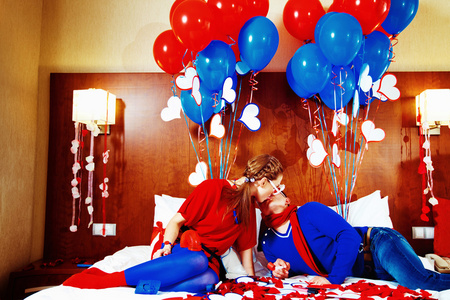 对幸福的夫妇身着红色和蓝色创辉气球背景在床上接吻照片