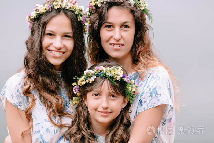 妈妈和两个女儿穿着白色裙子着花环的野花在湖边散步