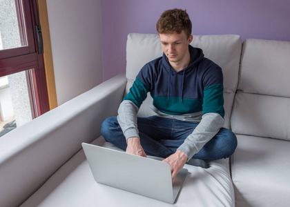 年轻男子坐在沙发前面一台笔记本电脑