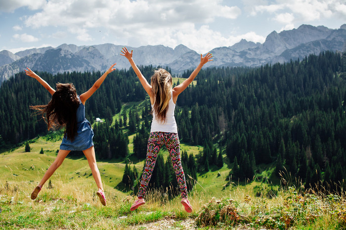 两个女孩在山背视图中快乐地跳起来