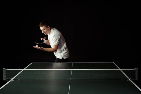 网球运动员与网球球拍和球在手站立在被隔绝的乒乓球桌在黑