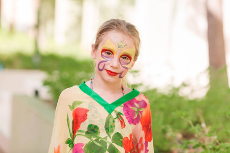 快乐的小女孩与面孔艺术油漆在公园里