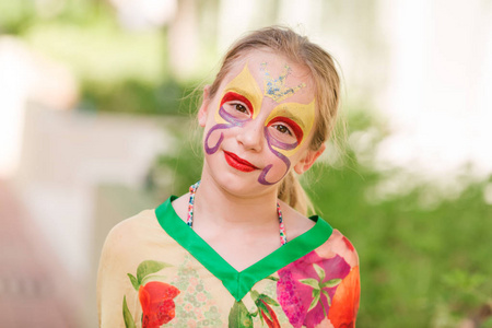 快乐的小女孩与面孔艺术油漆在公园里
