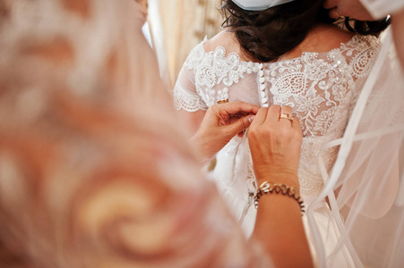 伴娘帮助穿的婚纱礼服的新娘在房间