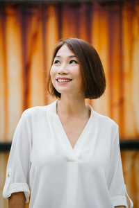 一个中年和迷人的中国亚裔妇女的肖像, 反对一个有创意, 艺术背景的锈色墙。她穿着时髦的休闲服 白色衬衣, 牛仔裤, 微笑着。