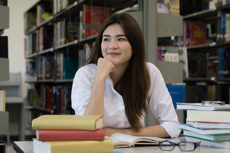 年轻漂亮的亚洲学生在图书馆看书时微笑着看着相机。教育理念