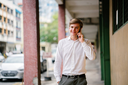一个年轻的白种人微笑的肖像。他穿着智能手机从事商务休闲。他年轻, 英俊, 上镜, 看起来高兴, 自信和兴奋